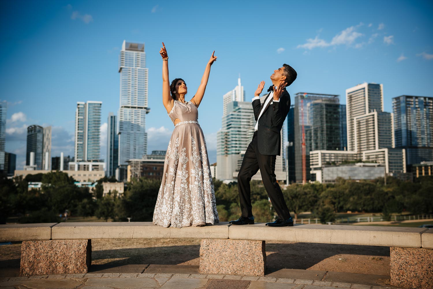 Goofy couple pose on concreate bench at Butler Park with downtown Austin behind