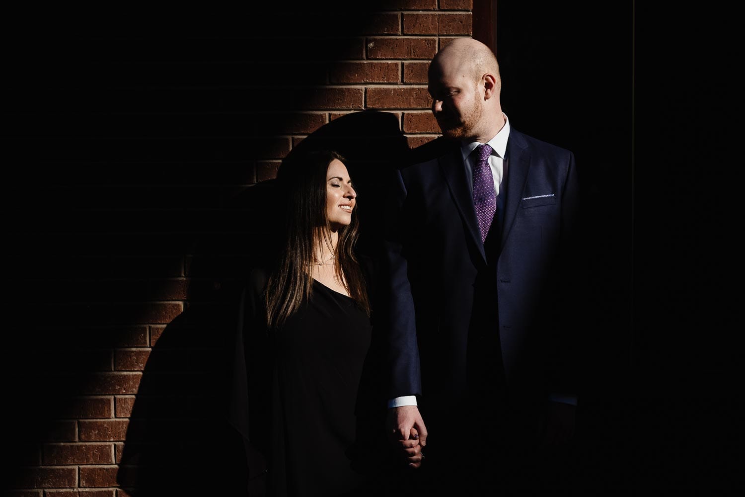 Engaged couple against brick wall at Pearl Brewery in beautiful light and shadow