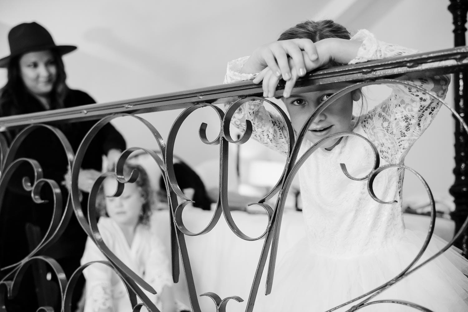 Flower girl peers through metal railing in a hotel room