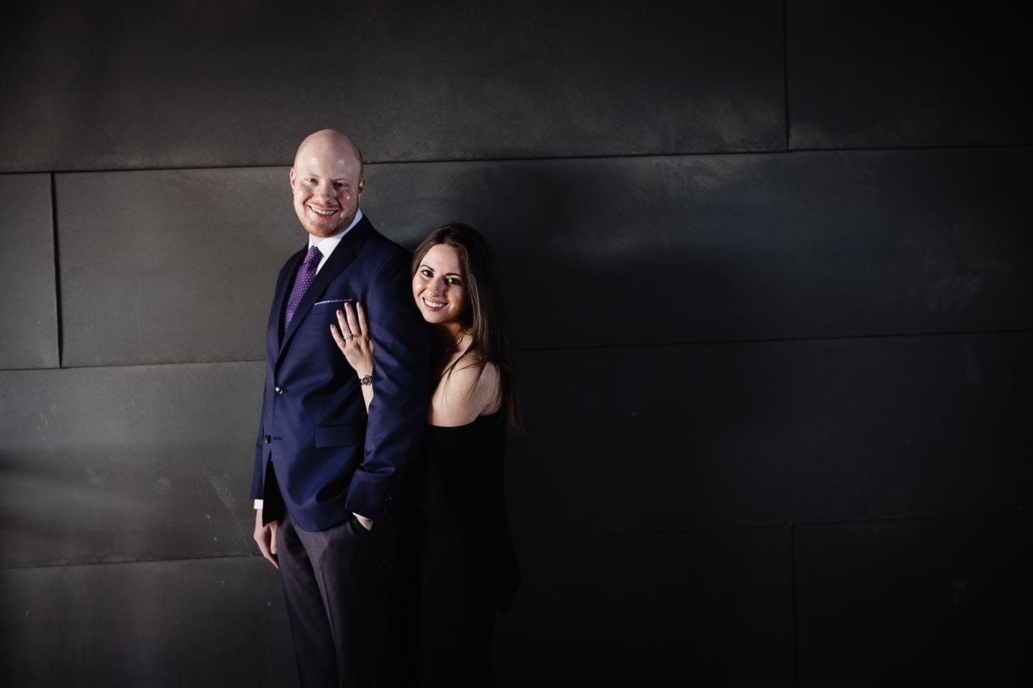 Striking couple in soft light pose against parking lot wall