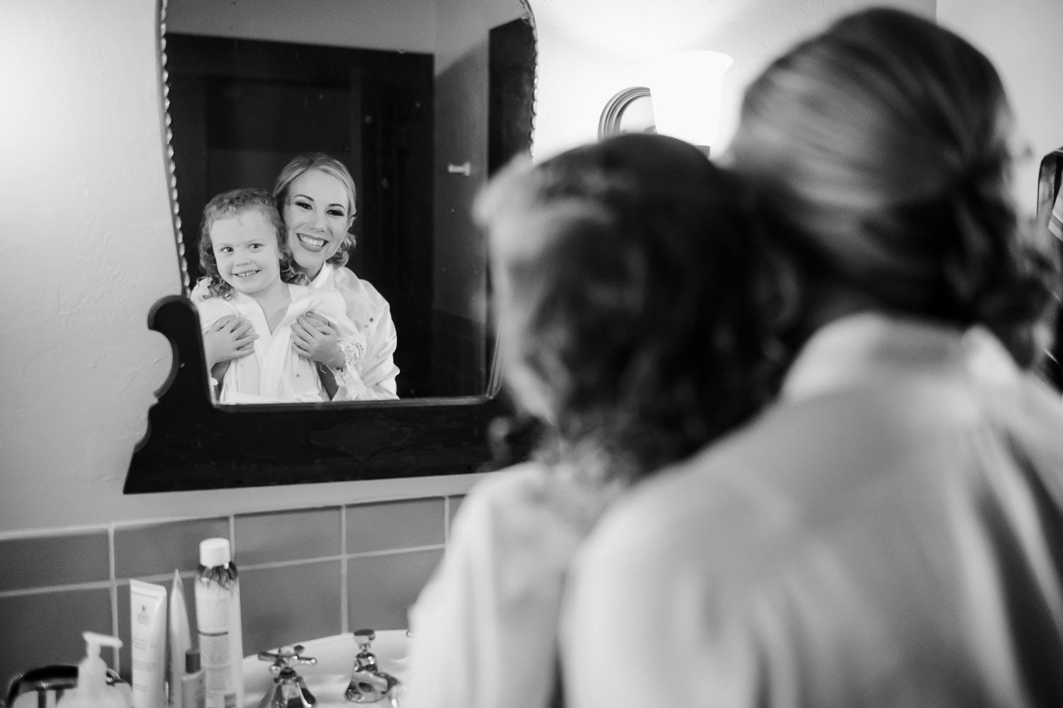 Kelsey the bride and flowergirl smile in mirror