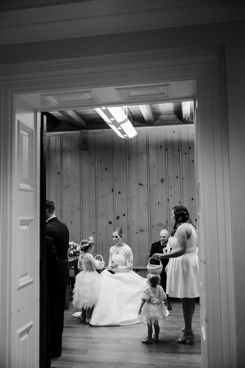 Photographed through the frame of a door shows the bride sitting with a flowergirl preceremony