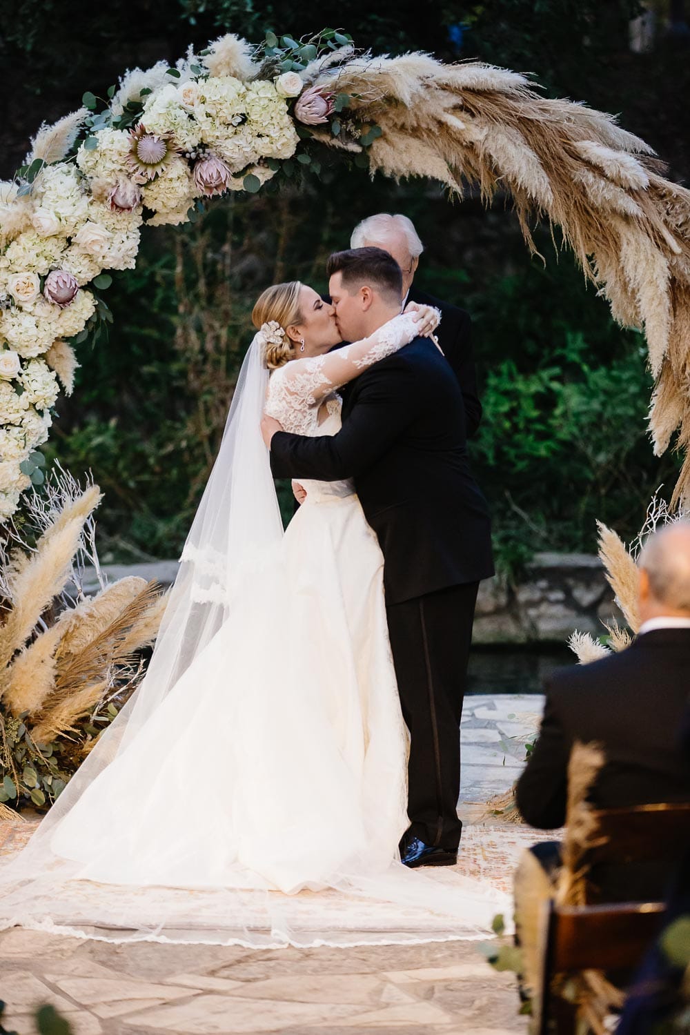 The couple enjoy their first kiss in front of a beautiful floral arrangement at The Witte Museum wedding
