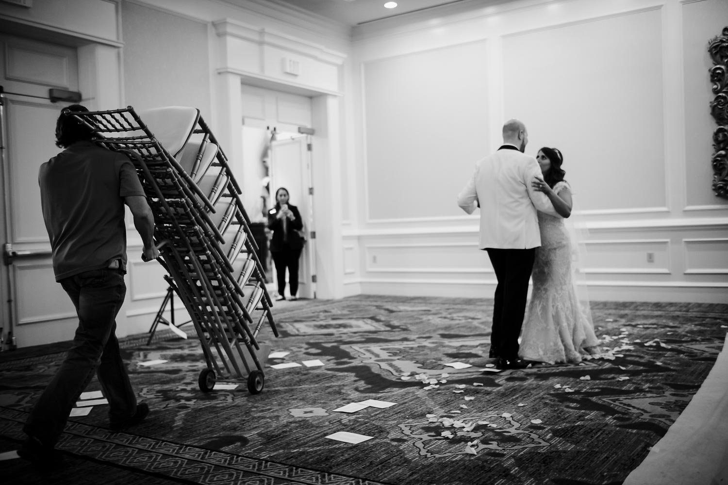 An interesting juxtaposition as the wedded couple practice first dance and chairs are pushed out of the ceremony to the reception ballroom