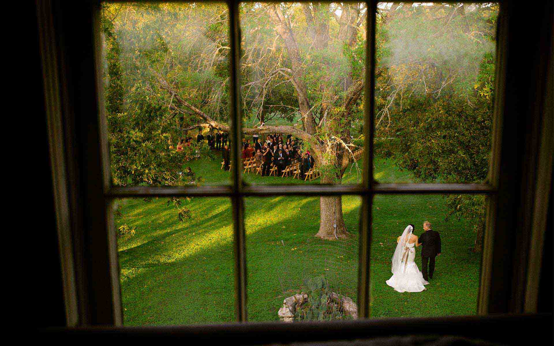 Shot-through-a-window-at-Don-Strange-Ranch-Texas-as-bride-walks-down-the-asile-with-her-father--photographed-by San Antonio wedding photographer Philip-Thomas