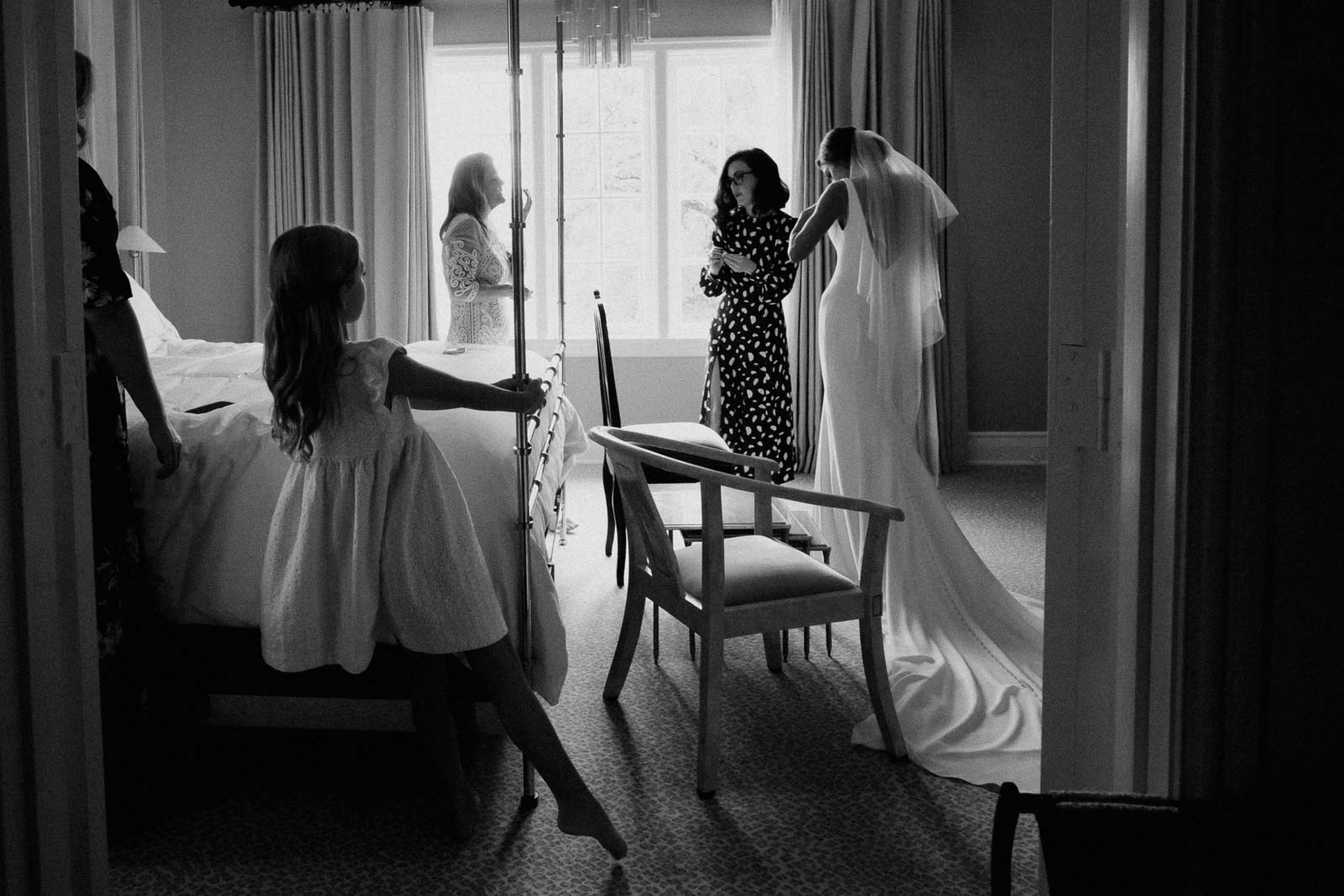 A flower firl watches a bride get ready by window light