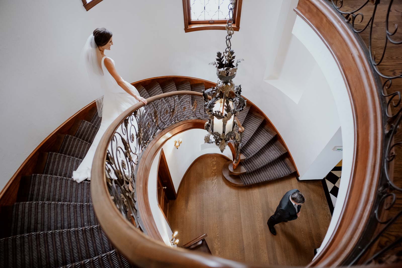 A bride greets her father in a first look down a spiral grand staircase