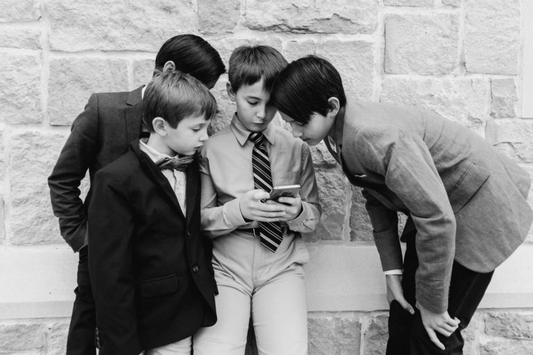 Boys gather and look at their devices against a church wall after a wedding
