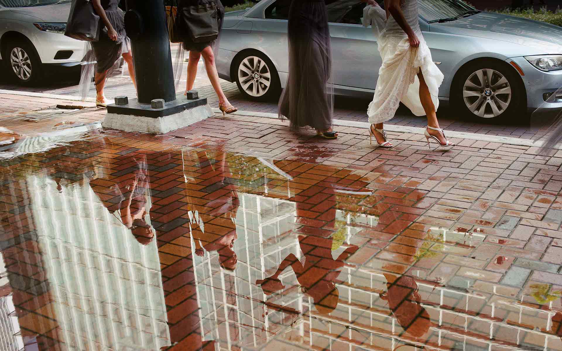 San Antonio Wedding Photographers Philip Thomas is a multi-award winning wedding photographer based in San Antonio serving Houston, Dallas, Austin, Galveston, South Texas. A WPJA award winning image. Bride and bridal party legs reflect in rain puddle, leave hotel through rain soaked streets in Houston, Texas.