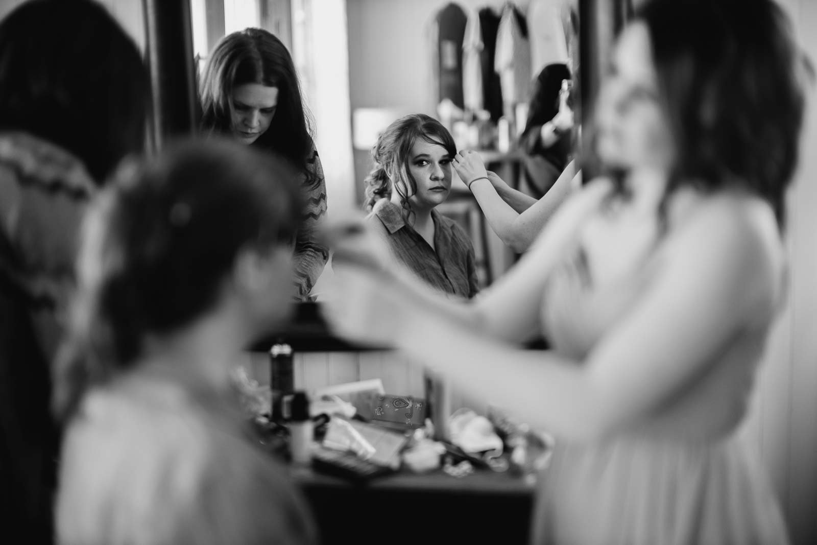 A bride looks in the mirror as a sister works on her hair
