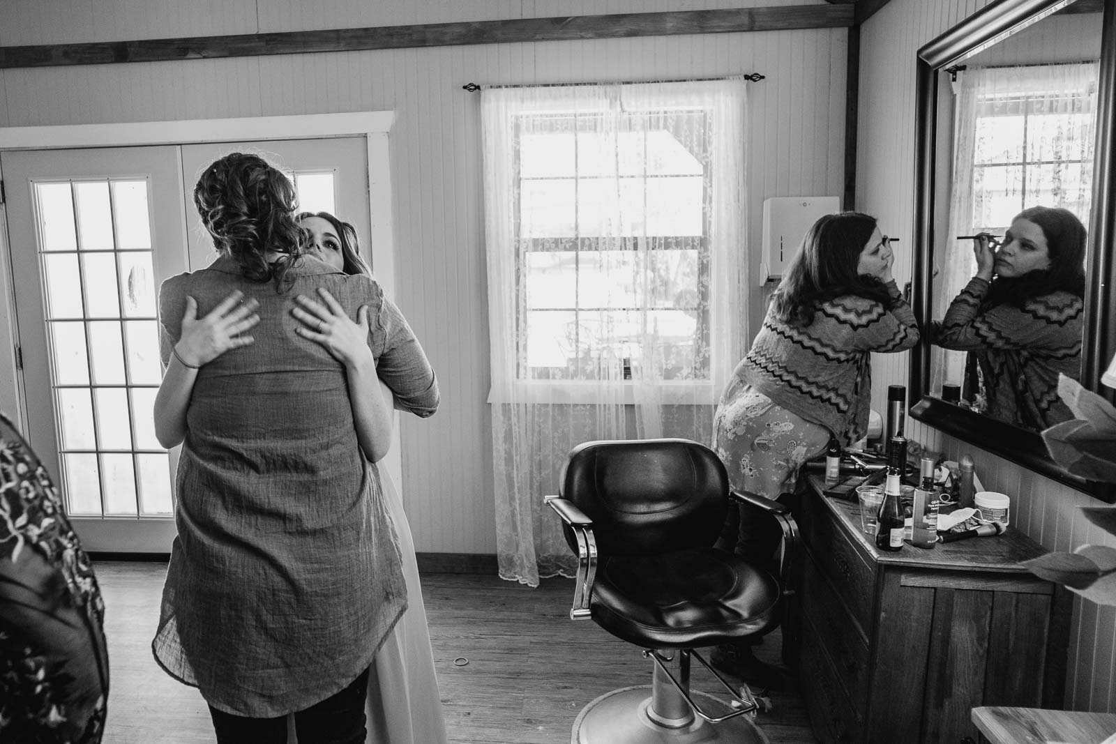  Sister applies make up in the mirror as sister in law bride and sister-in-law hug