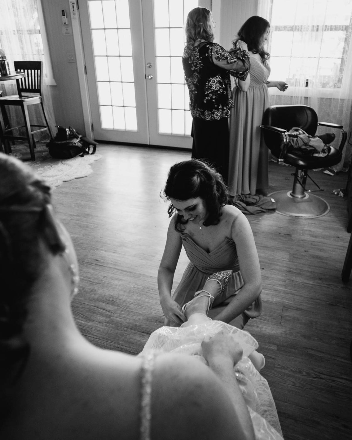 The sister-in-law puts on the brides shoe in the vertical shot with her mother and sister in the background at Spinelli‘s