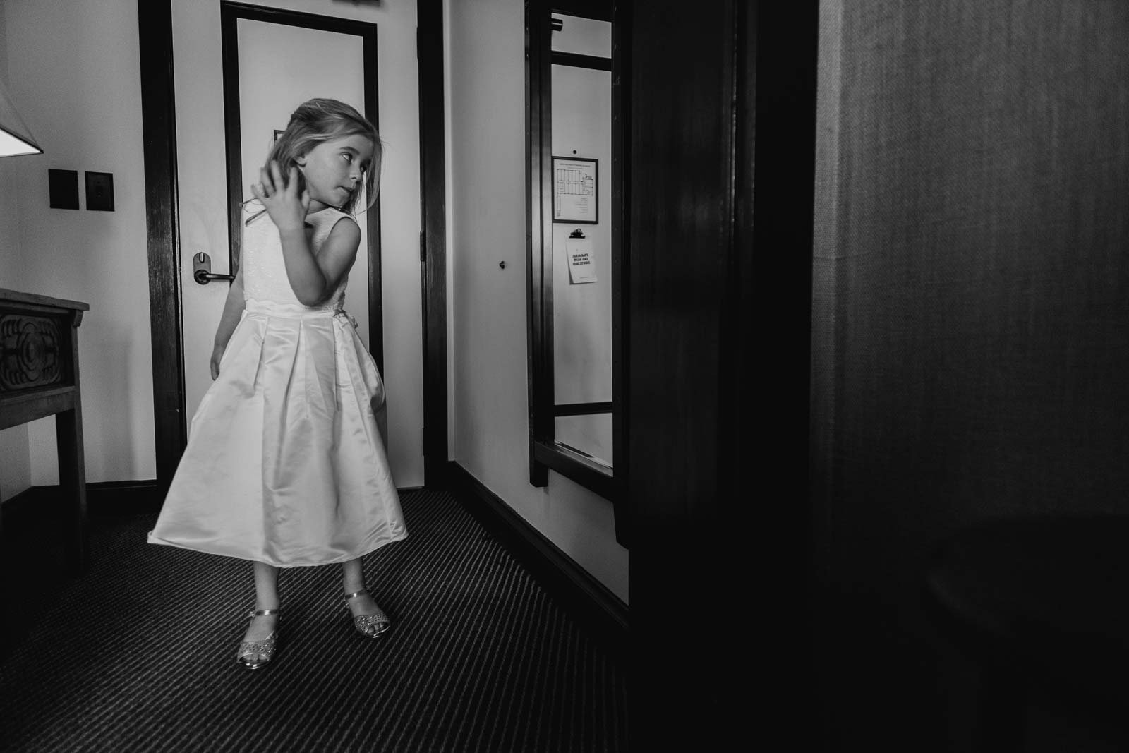 A cute little flower girl twirls in the mirror and catches her attention 