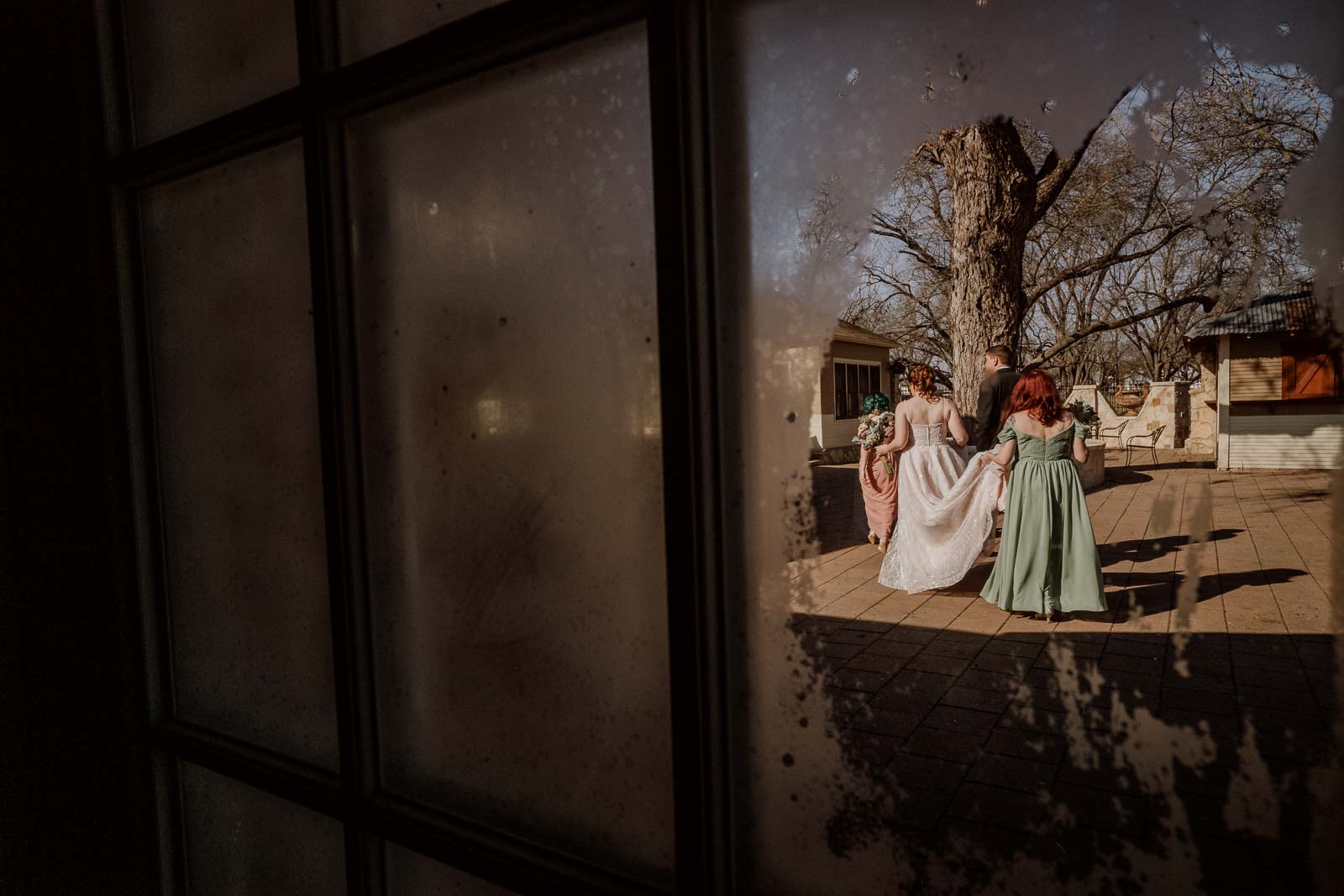 The bride and sister of the bride holds her dress as she walks towards the church photographs through the layering of a window