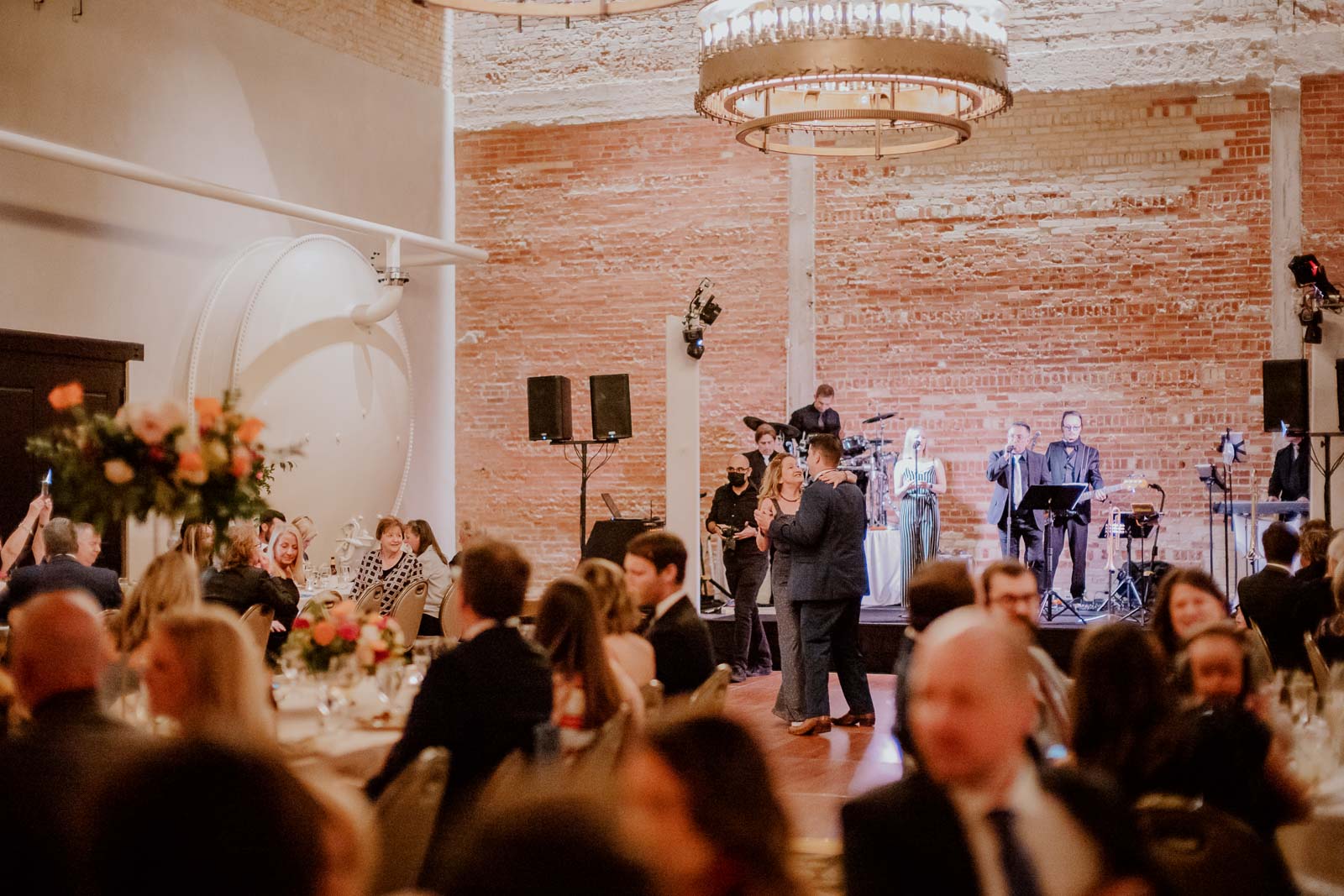 The groom and his mother have a first dance at the run in a wide angle shot as guests look on