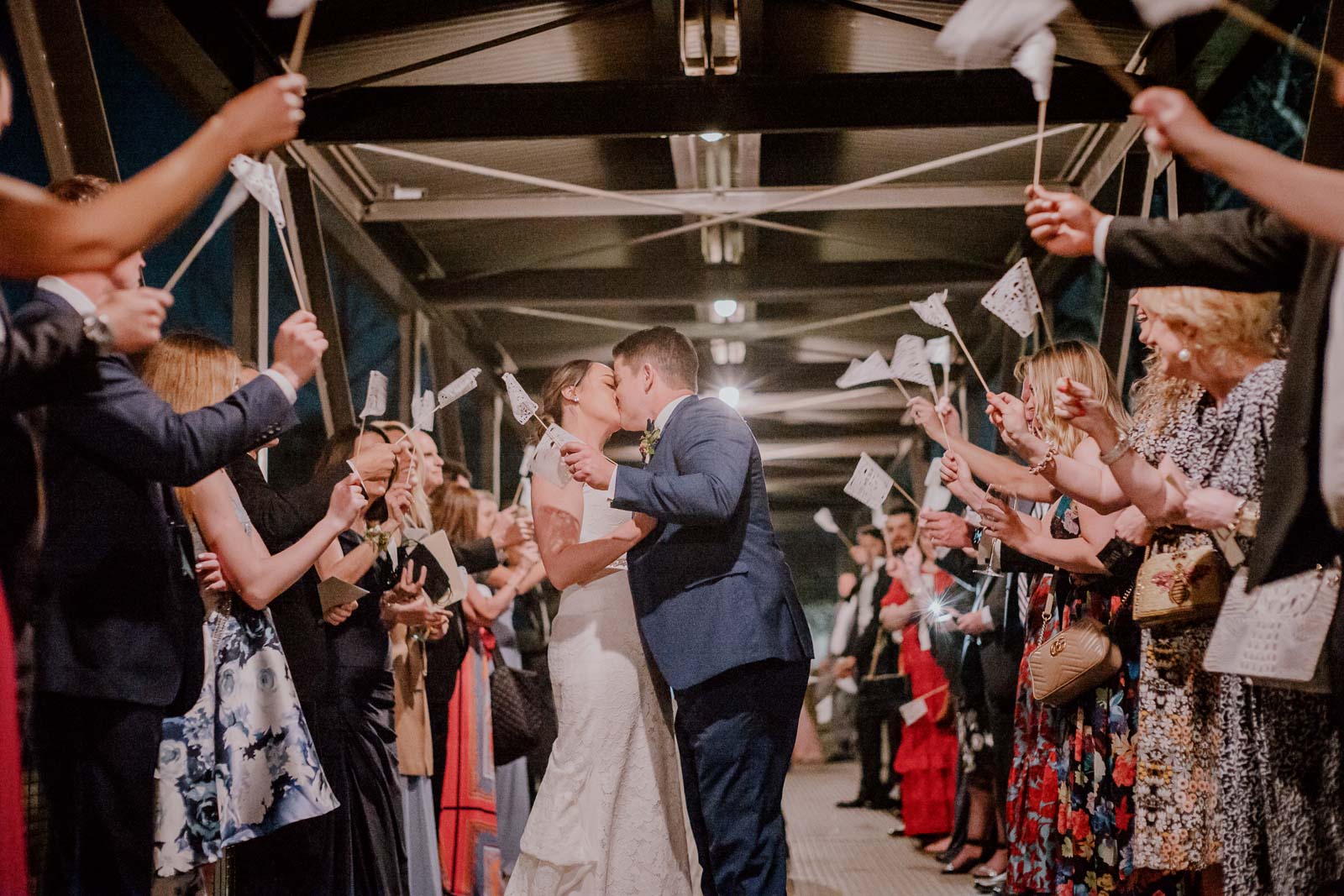 Sparklers and flags are raised high up into the air as a bride and groom make the exit and kiss just outside Hotel Emma