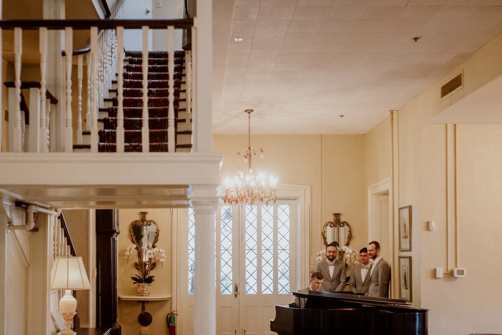 A wide shot of the stairwell coming down with the eye leading to the room playing the piano