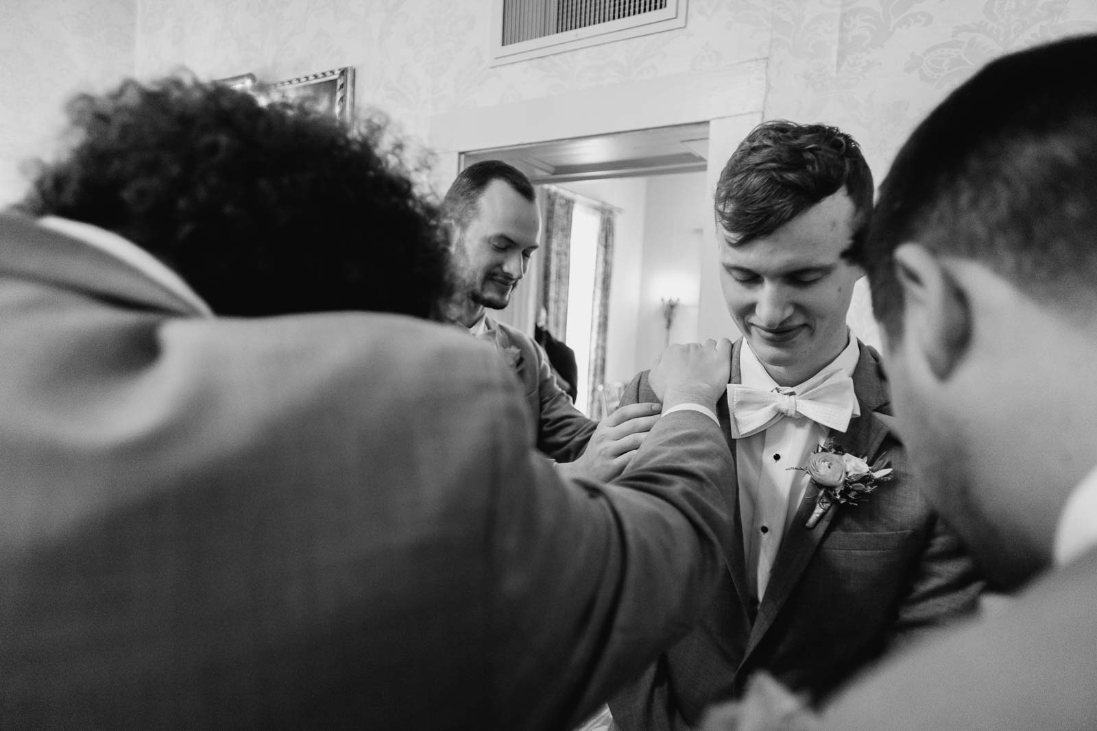 And a prayer circle groomsmen rest hands on his shoulders