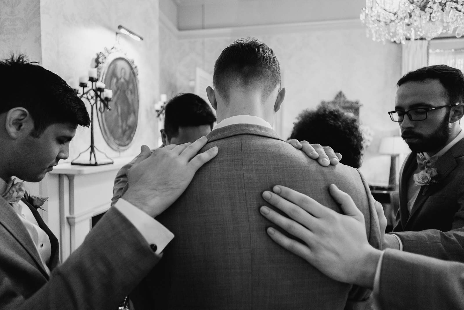 Behind the groomsman as hands are rested on his back