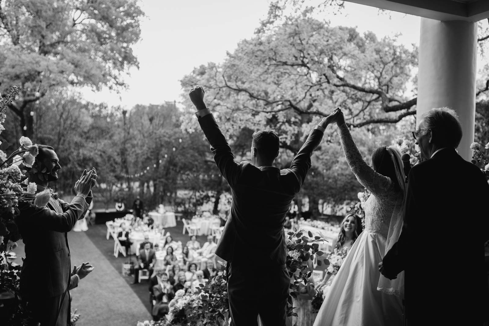 With their hands raised a photograph from behind the bride and groom as they celebrate their marriage towards the crowd celebrates