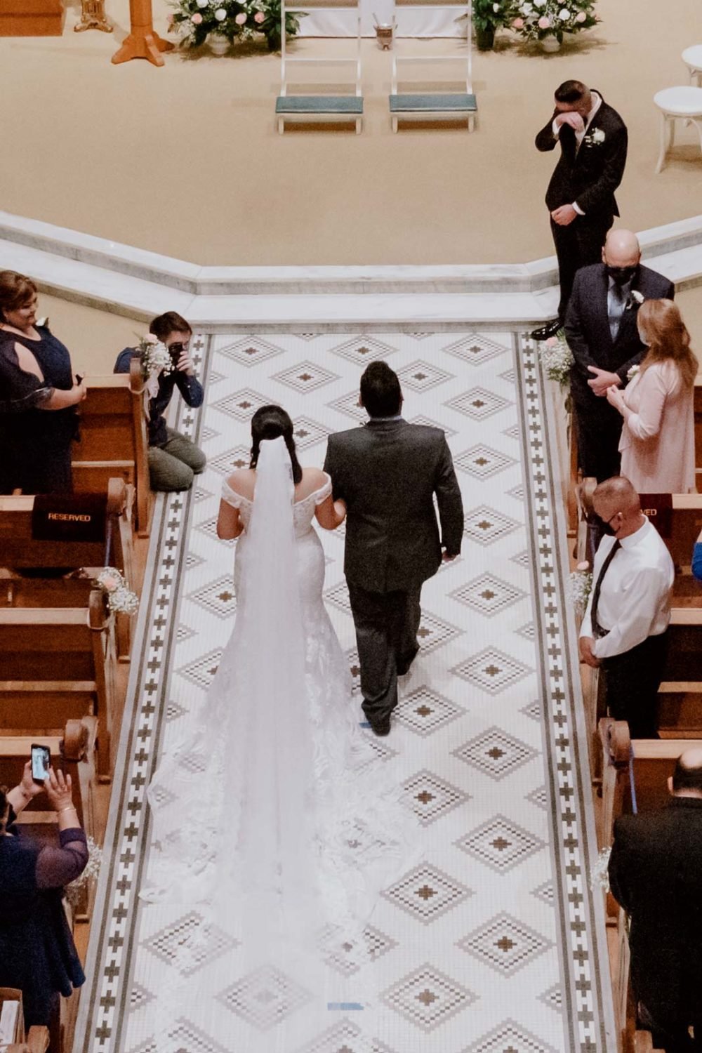 The bride walks down the aisle as the groom wipes away a tear from his eyes at  Sacred Heart Chapel-Leica photographer-Philip Thomas Photography