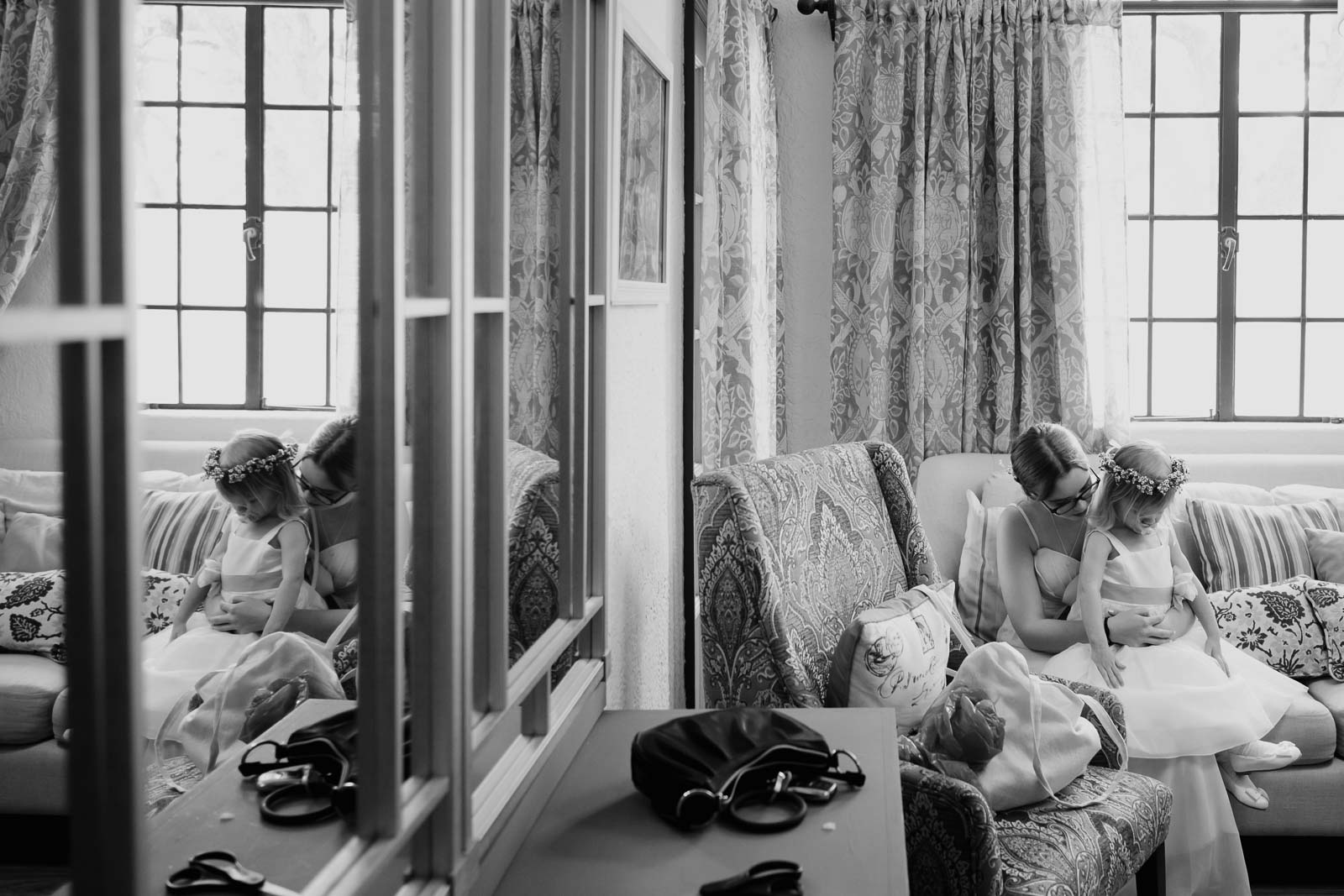 In a mirrored photo two young bridesmaids cuddle on the sofa at the veranda