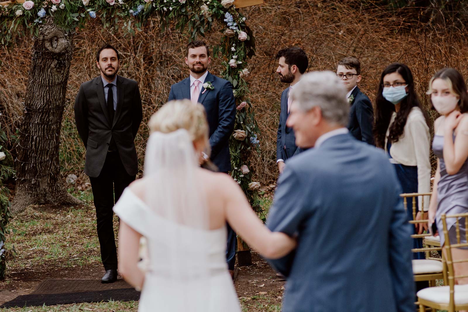 During the ceremony a close personal friend books the bride down the aisle as guests look on with masks on their faces join Covid