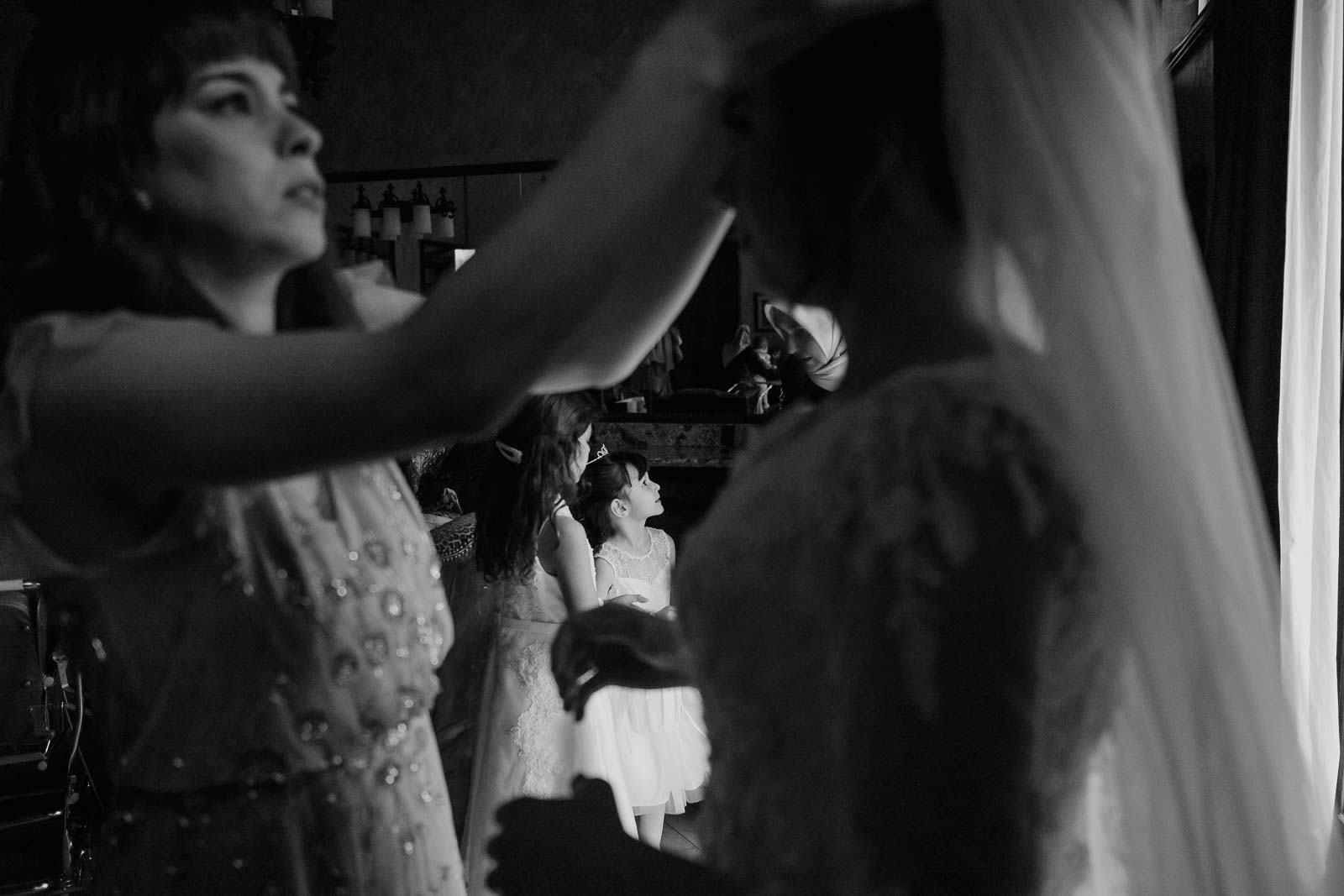 A flower girl looks up towards her mother as the bride’s friend fixes her veil