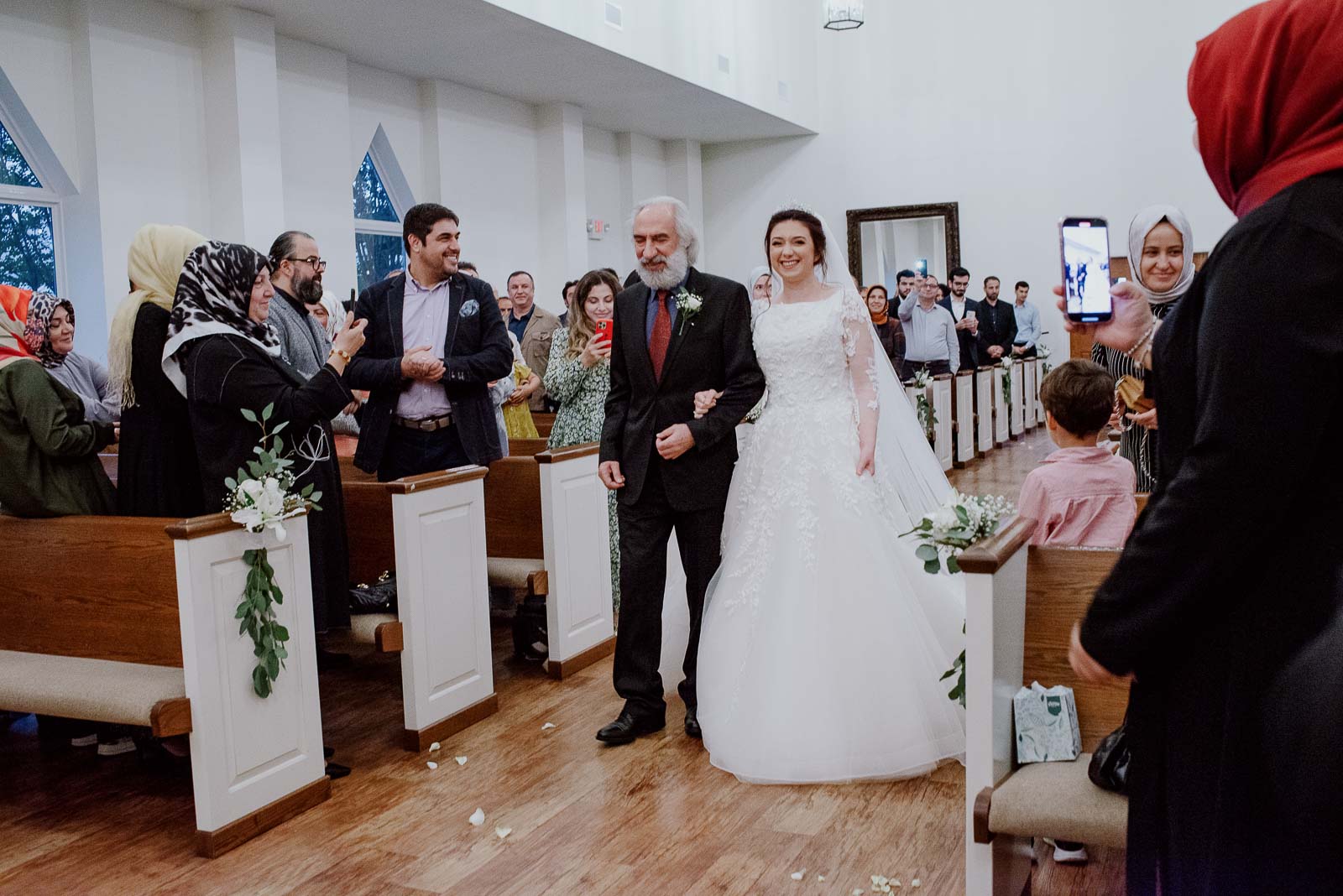 Father of the daughter and Bride walk down the aisle together building smiles cement by family and friends cheering