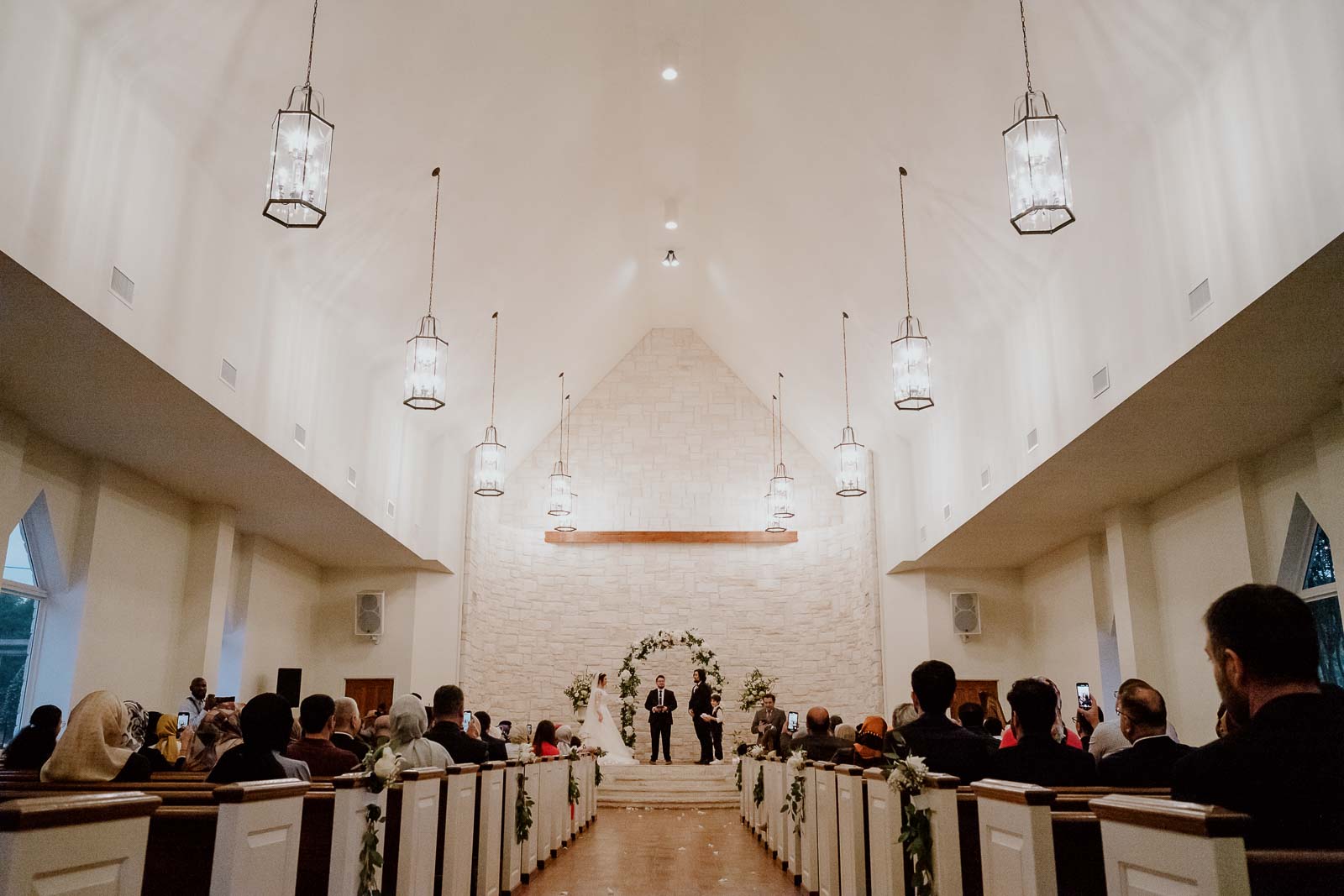 A wide angle shot of the hanging lights and the guests attending the wedding during the ceremony at Briscoe manner