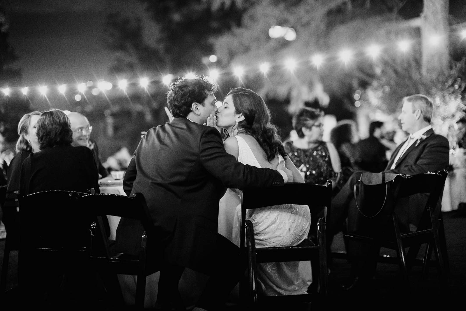 Couple steal a kiss during wedding reception under string lights at The Witte Museum Wedding photographer San Antonio Wedding Documentary Photojournalist Leica Wedding Photographer Philip Thomas
