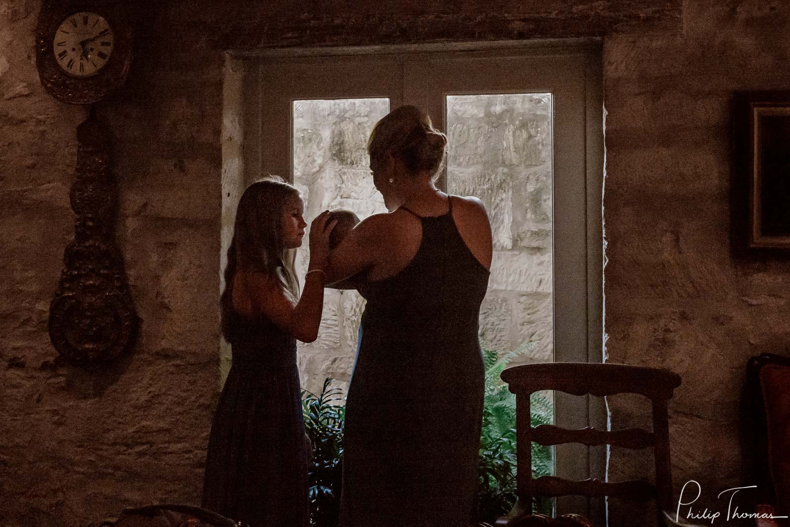 Daughter of the groom kisses a baby with bride silhouetted against a window at Club Giraud Wedding Reception San Antonio weddings Philip Thomas Photography