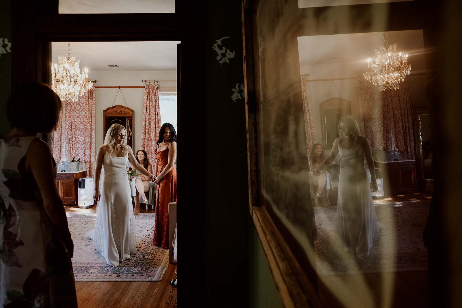 The bride holds a bridesmaid's hand as she is shown in the reflection and her mother on the left.