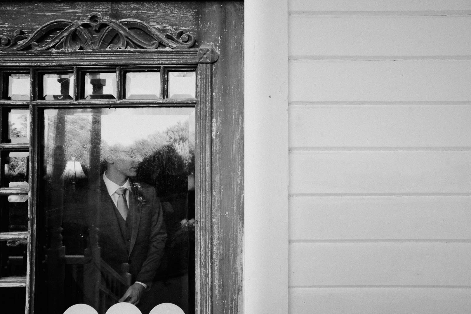 The groom stands at a window and is slightly obscured