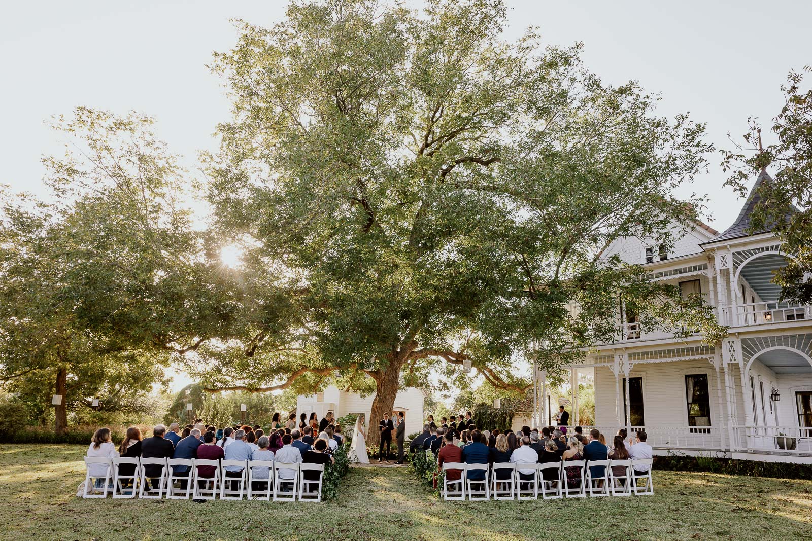 A super wide angle view of a wedding taking place with the old house on the right and oak tree in the middle at Barr Mansion