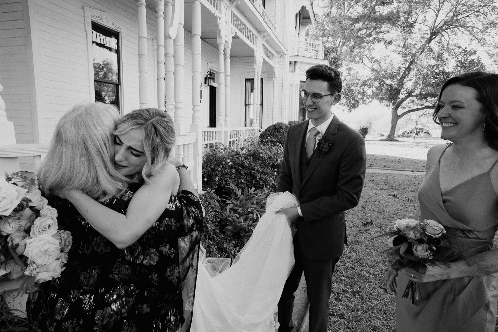 An emotional hug with the bride and a family member as the groom holds the bride's dress