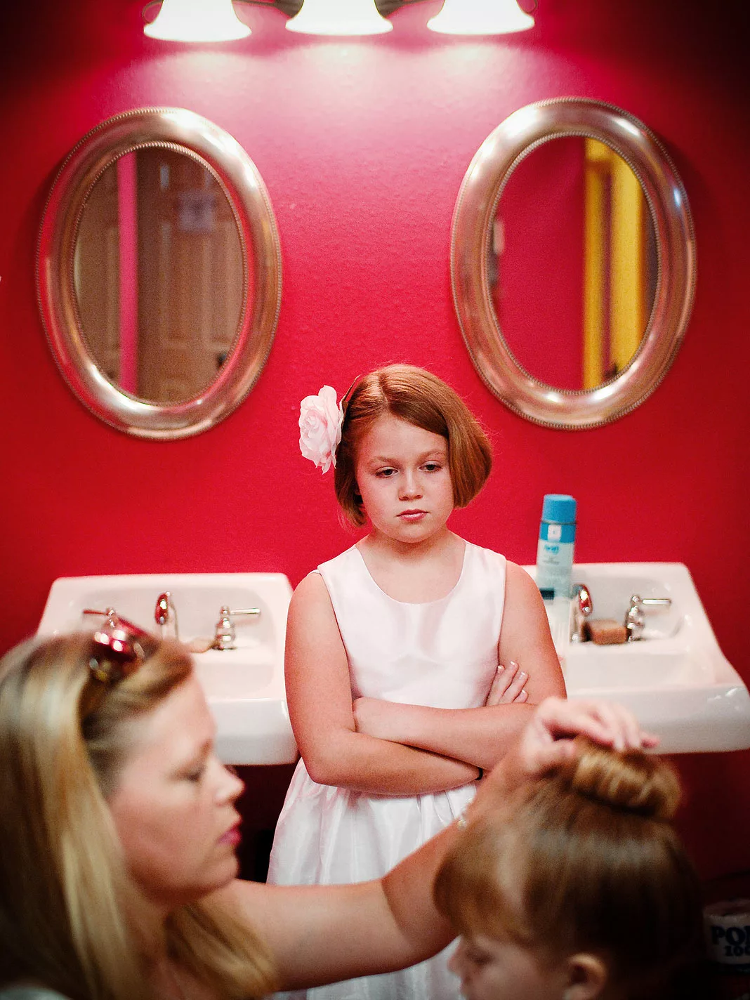 A jealous flower girl stares down her sister in a pink room
