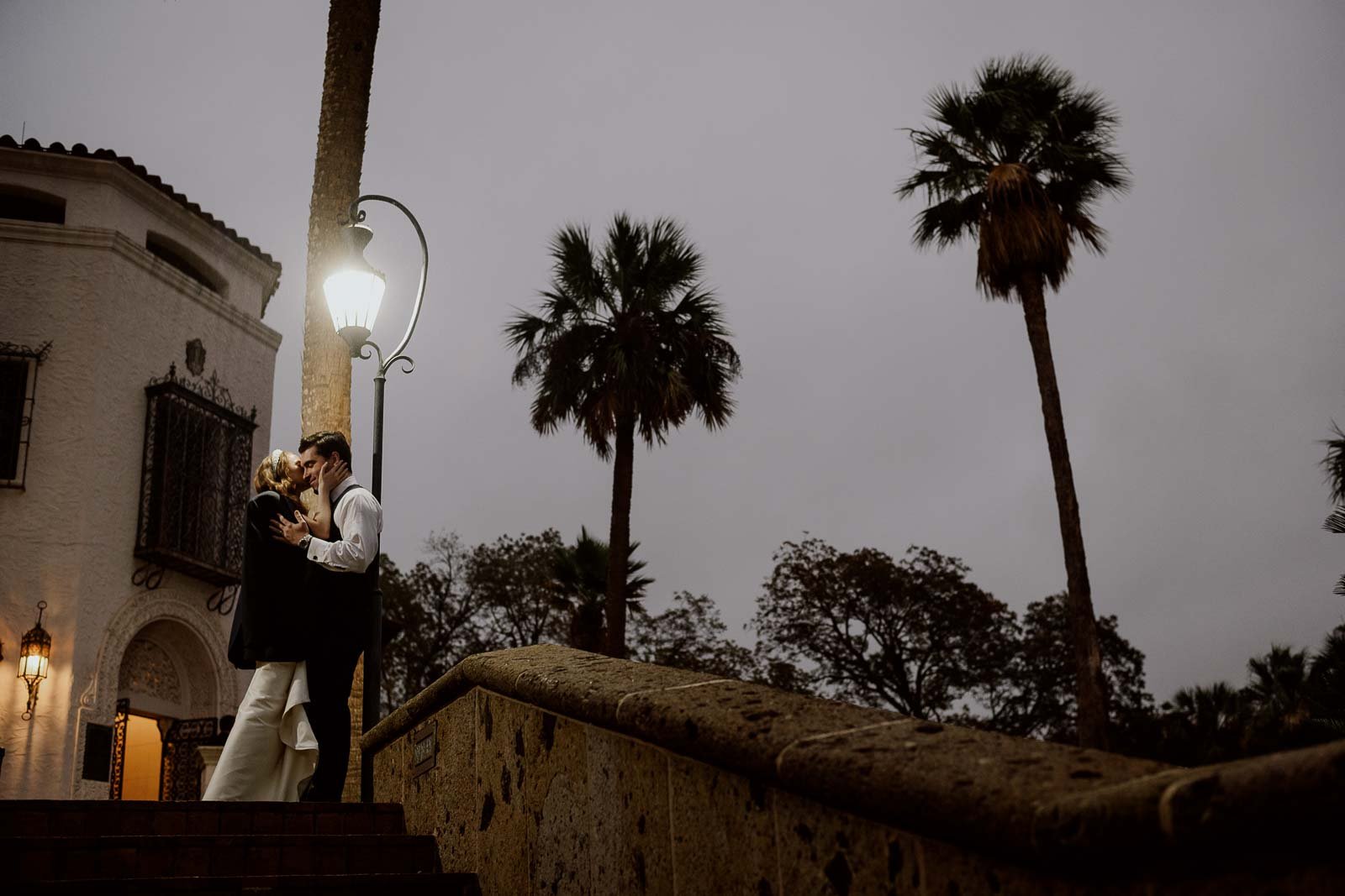 The newly married couple photographed at the McNay Art Museum photographed at dusk under the lamp with palm trees against the sky