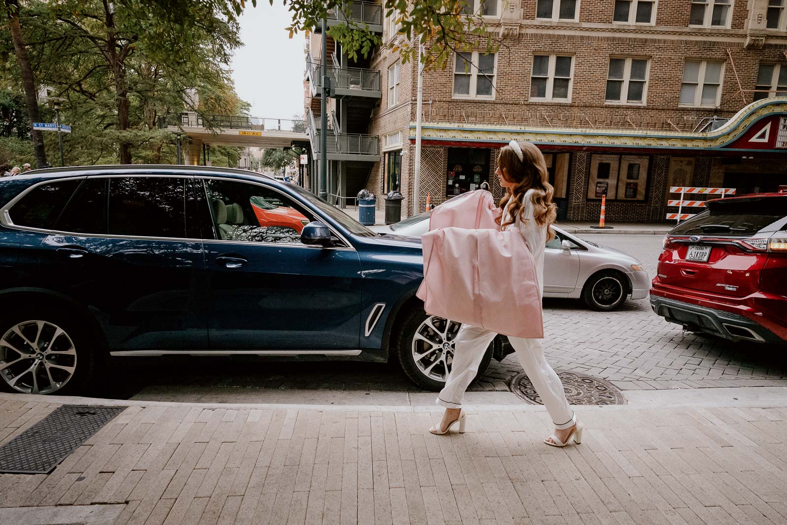 A bride walks the street with her bridal gown draapd over her arms