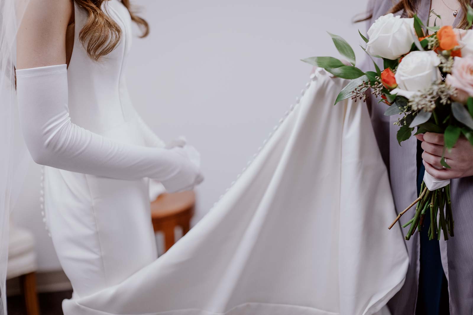 A bridesmaids helps the bride holding her dress