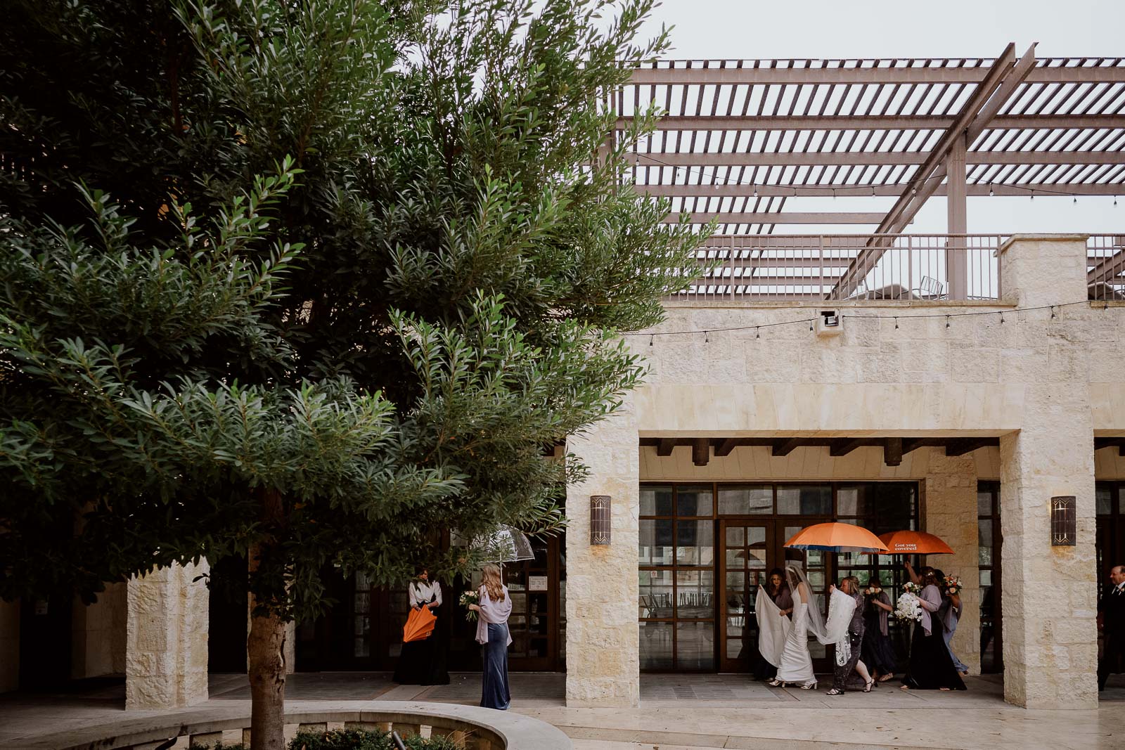 Orange colored umbrellas protect the bridal party from the rain on the grounds of San Fernando Cathedral in San Antonio Texas