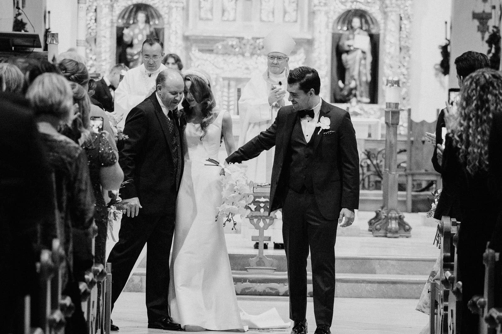 The bride hugs her father and the groom leads the way down the aisle at a catholic wedding ceremony in San Antonio