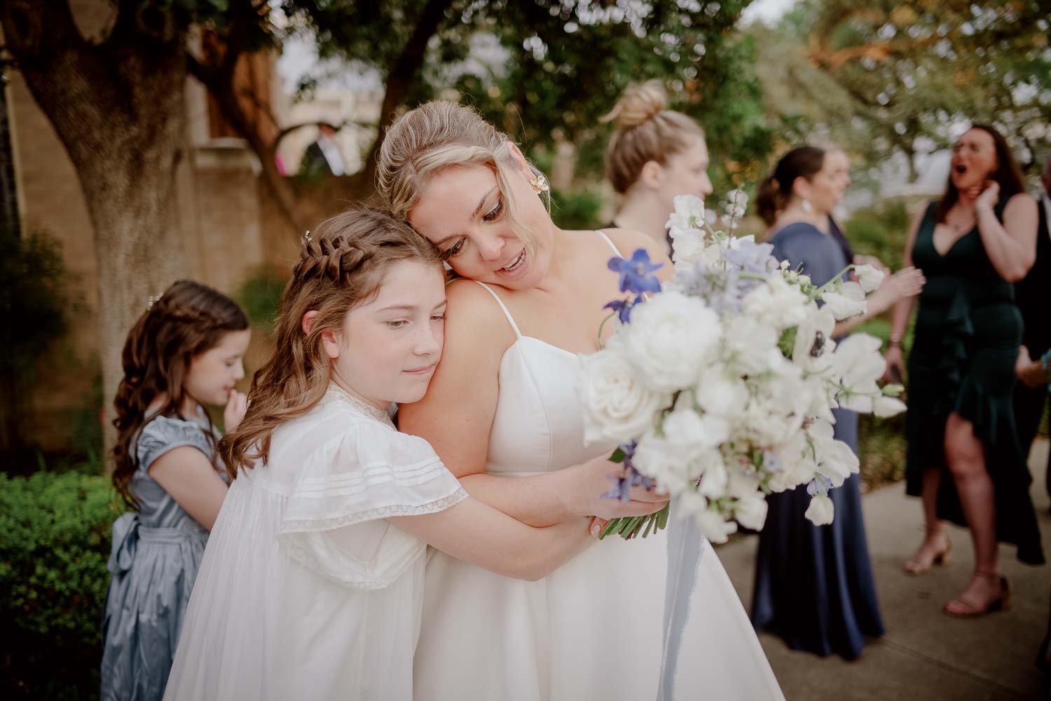 A flower girl and bride embrace after she ties the knot on the steps of Christ Episcopal Church wedding ceremony san antonio-L1003740