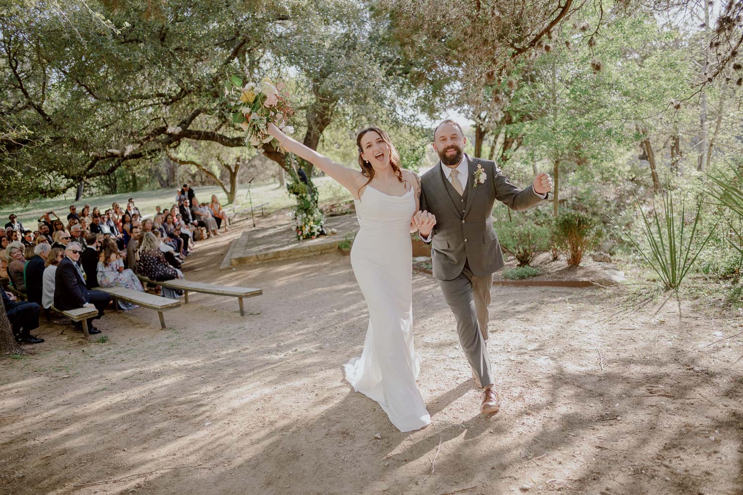 A newly wedding couple ecstatically raise their arms at the wedding ceremony The Retreat at Balcones Springs_Wedding photographer-Philip Thomas-L1007433