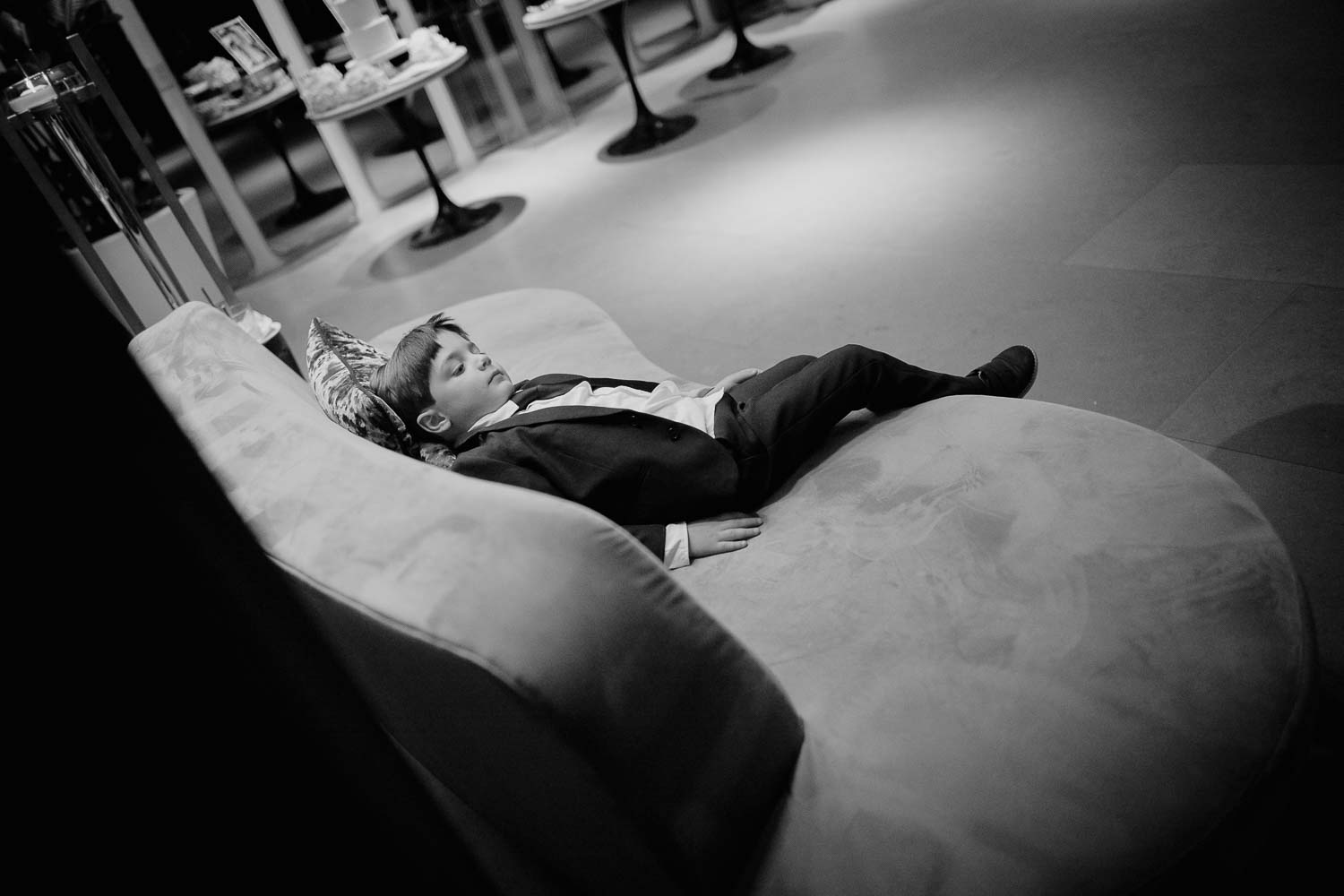 A boy rests on a sofa during a wedding reception