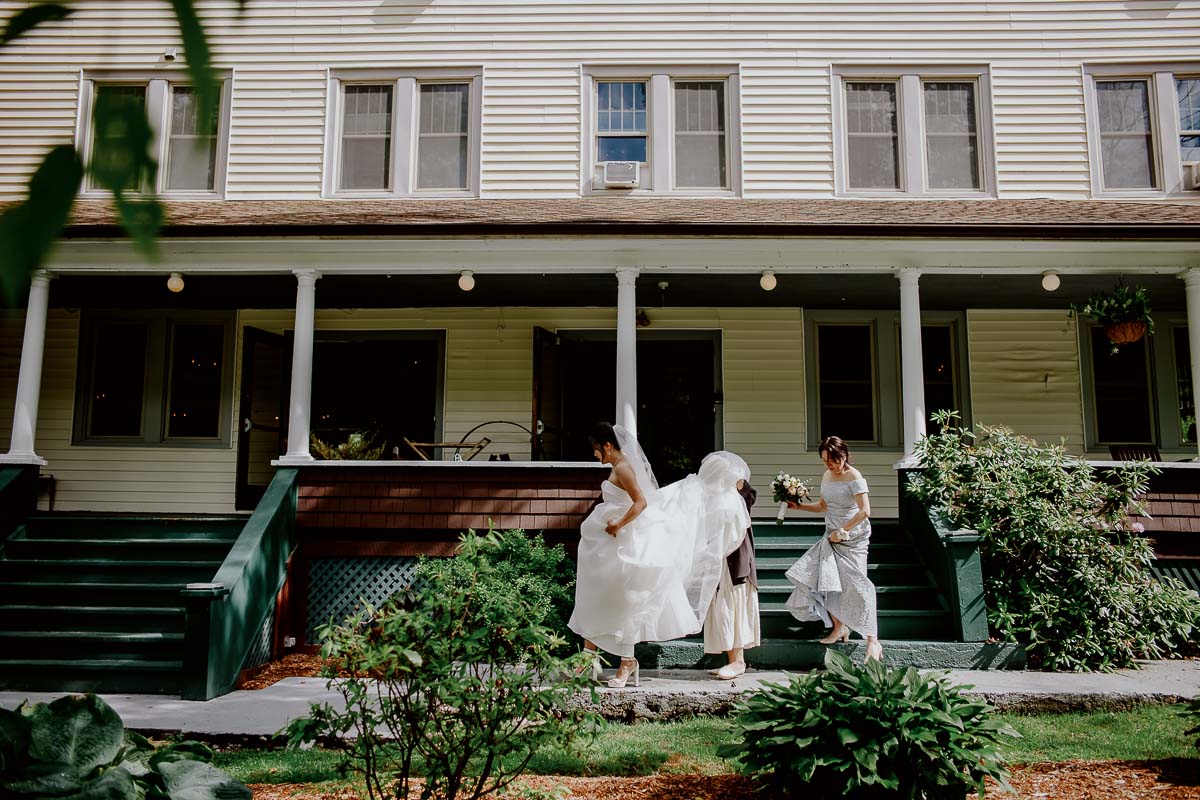 The mother of the bride and an assistant hold the wedding dress at the steps of The DeBruce in Livingston Manor wedding ceremony and reception in New York - Leica photographer Philip Thomas Photography