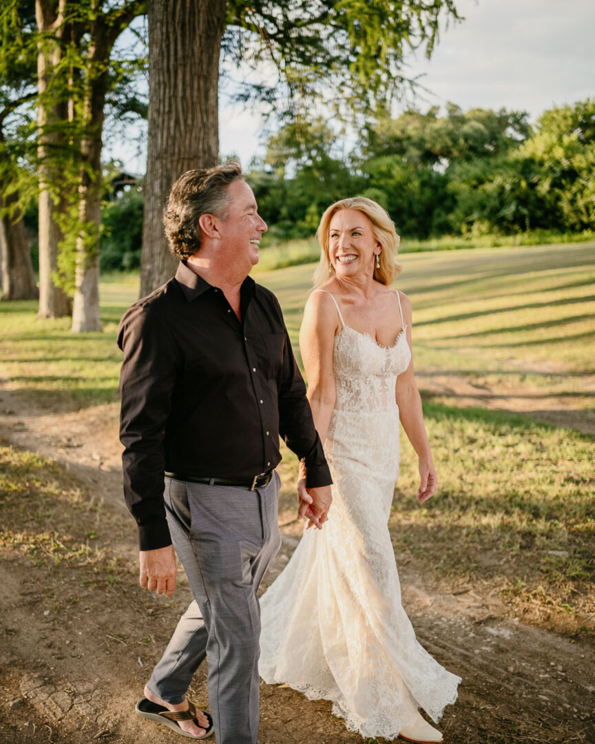 a man and woman holding hands and walking on a dirt path