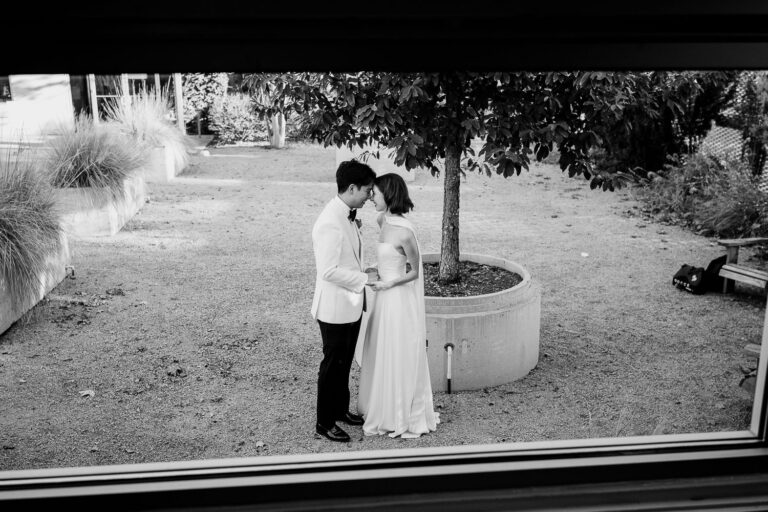 Bride walking in elegant white dress at The Ice Plant Bldg in La Grange photographed through the window in grooms dressing room