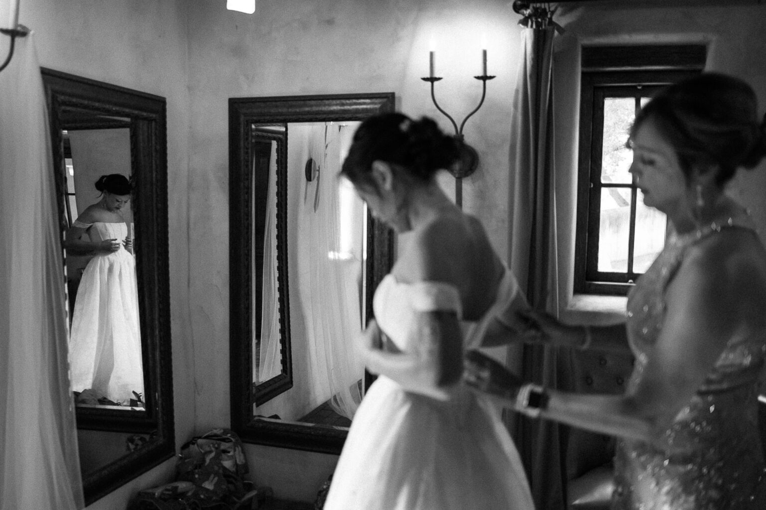 Bride preparing with assistance in mirror.