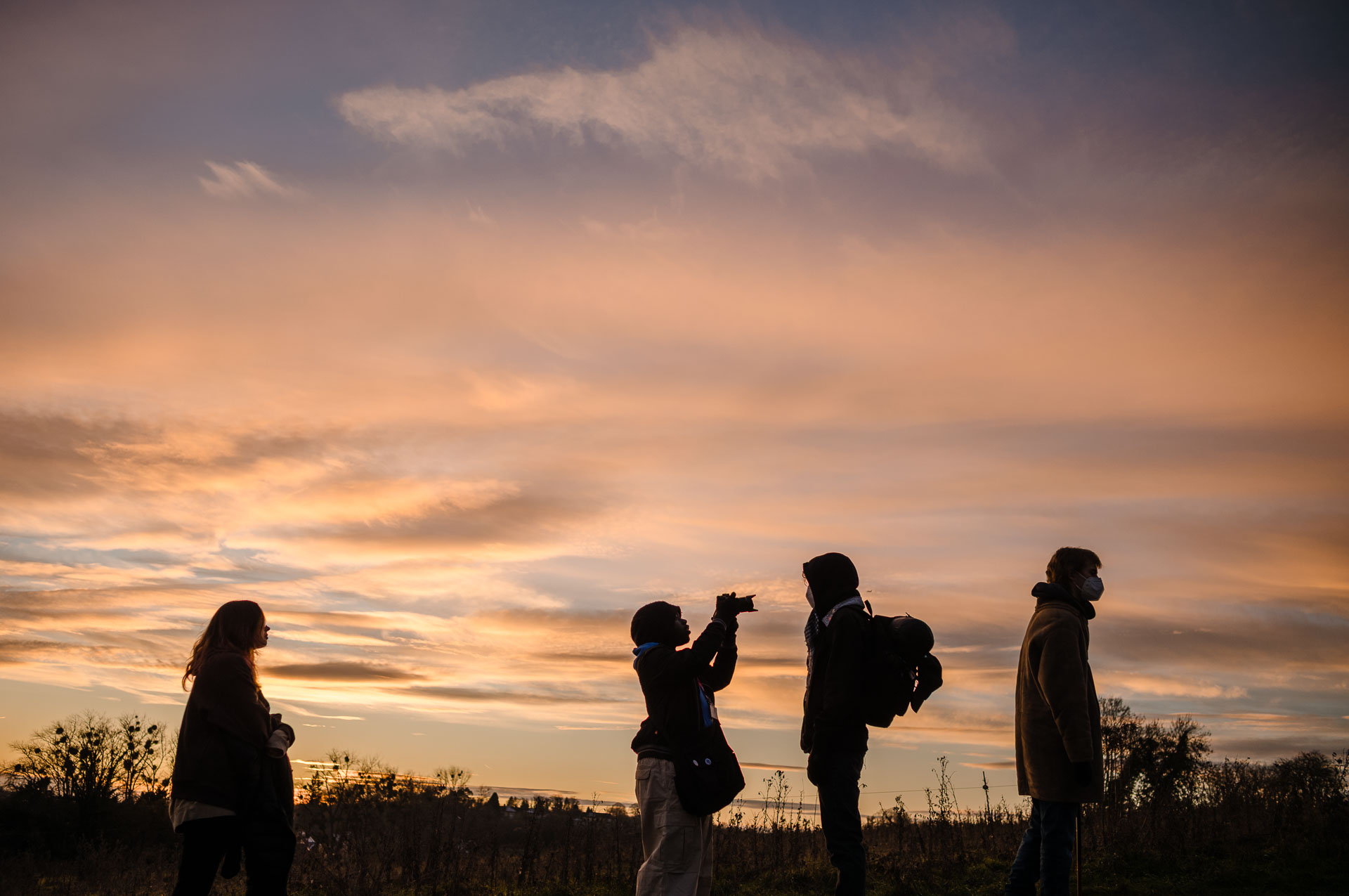 Silhouettes of crew and talent standing in a field at sunset during an outdoor shoot